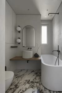 Modern minimalist bathroom with a white bathtub, wooden vanity, and marble floor tiles.