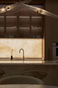 A minimalist modern kitchen featuring marble countertops and backsplash with a sleek, white faucet and lighting design above.