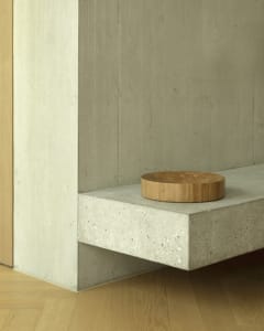 A minimalist interior design featuring a concrete shelf with a circular wooden object on it.