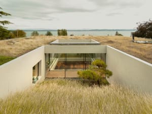 Modern concrete house with glass walls overlooking a lake.