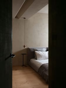A modern minimalist bedroom featuring a bed with a low-profile fabric headboard, white bedding, and wood flooring.