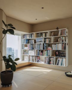 A modern floating bookshelf filled with books and decorative items, positioned by a large window with views of a city skyline