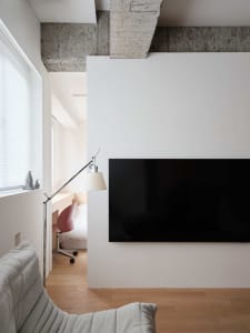 Modern living room with a concrete wall, minimalistic furniture, and a sleek black TV.