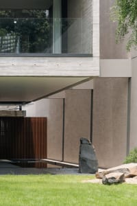 Modern house with concrete walls, glass window, and stone sculpture in the garden.