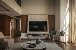 A modern living room features sleek, minimalist furnishings with a marble coffee table, wooden chairs, and a tile fireplace.