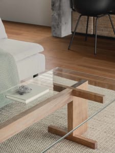 A modern living room with a glass coffee table and wooden accents.