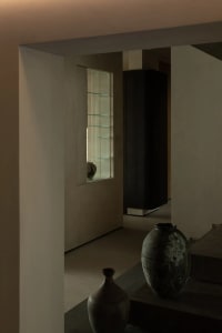 Modern living room with concrete walls and floor, featuring a large vase and a glass display case.