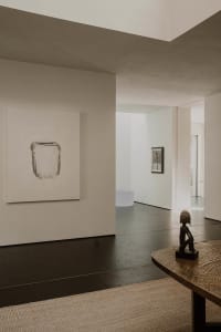 A minimalistic industrial interior with concrete flooring and walls, featuring a wooden table with a metallic base and a scul