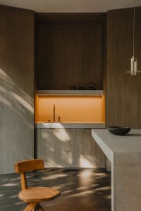 A minimalist kitchen featuring concrete countertops and wood cabinetry.