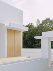 A modern minimalist white exterior featuring wooden doors and a sleek design.