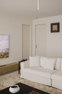A minimalist living room with a white canvas couch, wooden flooring, and white walls.