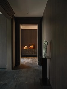 Interior design featuring a minimalist entrance with dark wood paneling, a table with a sculpture, and a sideboard with a pie