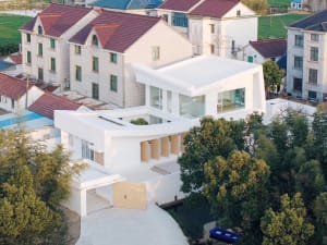 Modern residential building with a white stucco exterior surrounded by greenery.