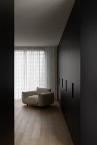 A minimalist residential space featuring a white armchair and sheer curtains.