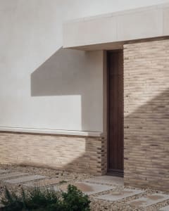 A modern house entrance featuring brick and stone render, with a wooden door and a concrete path.