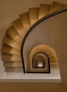 A modern, curved wooden staircase with a dark metal railing.