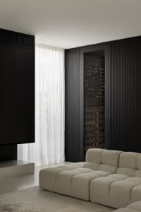 A modern living room featuring textured fabric sofas, a large screen TV, and a glass door wine cellar.