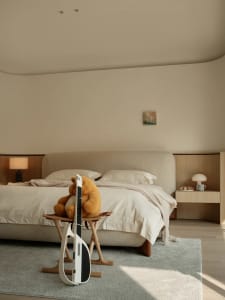 A minimalist bedroom with a beige upholstered bed, wooden nightstands, and a light blue rug.