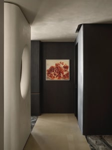 A minimalist corridor with dark wooden walls and stone flooring, featuring a framed painting of a pomegranate interior.