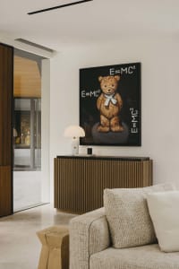 Modern minimalistic living room featuring a wooden sideboard adorned with a framed painting of a teddy bear with the equation