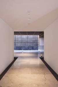 Long, spacious entrance hall with smooth marble tiles, leading to a black-framed glass wall.