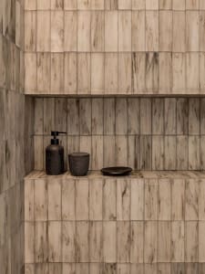 Modern bathroom featuring marble tiles with integrated storage shelves and small black items.