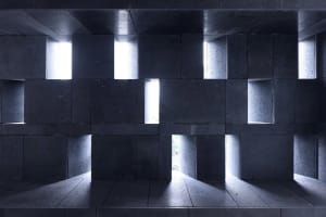 A modern interior space with concrete walls and light shining through windows.