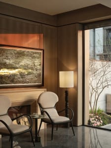 Modern living room with wood paneling, two beige upholstered chairs, and a floor lamp casting a warm light.