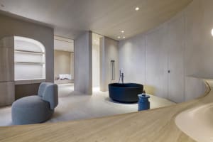 A minimalist bathroom with a round blue bathtub and concrete walls and floor.