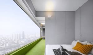Minimalist bedroom featuring clean concrete walls and a large window overlooking a cityscape.