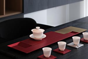 A beautifully arranged tea ceremony set featuring ceramic cups and bowls on a red tray.