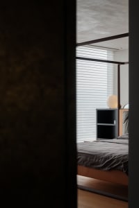 A modern minimalist bedroom with a bed, nightstand, and lamp.