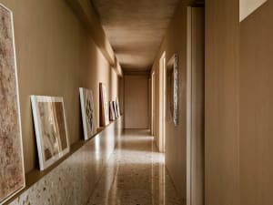 A minimalist corridor with a concrete wall and terrazzo floor, showcasing abstract art hanging along the walls.