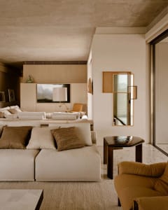 A minimalist living room featuring concrete walls and furniture with earthy tones and textures.