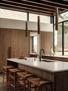 Modern interior with wooden cabinets, hanging lamps, and a central island with a marble countertop and sink.