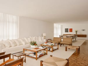 Modern minimalist living room with white sofa, wooden coffee tables, and abstract art hanging on the wall.