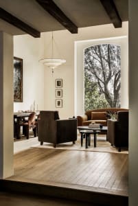 A modern living room with concrete walls and wooden flooring. Features include a large window, comfortable seating, and minim