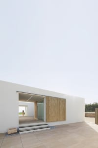 Modern minimalist exterior of a building with a concrete wall and wooden shutter.