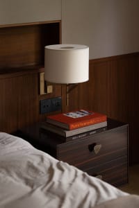 A minimalist bedroom featuring a wooden nightstand with books and a lamp.