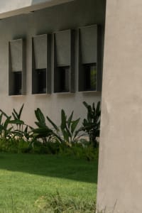 Modern architectural windows set in a concrete wall, surrounded by greenery and grass.