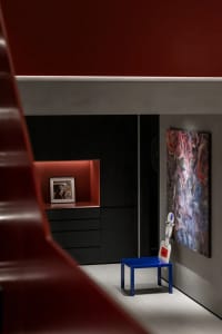 A modern living room with dark furniture, red accent wall, and abstract art.