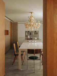 A modern kitchen and dining area featuring a metallic dining table and a crystal chandelier hanging above it.