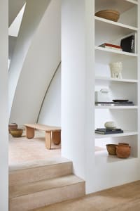 Modern staircase made of wood and concrete with minimalist design aesthetics, featuring a built-in shelf with books, vases, a