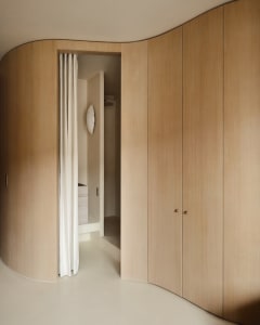A modern minimalist wooden closet system with curved doors and a white curtain.