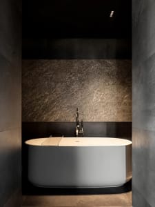 Modern minimalist bathroom featuring a metallic tub and dark stone walls.
