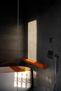 A minimalist bathroom featuring a white bathtub with an orange faucet, set against a dark gray granite wall.