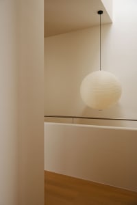 A black-wire paper lamp hangs from the ceiling in a modern stairwell.