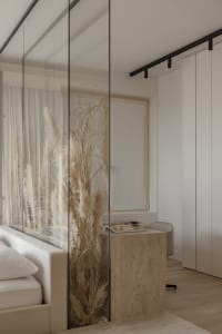 A modern minimalist bedroom featuring a wooden bed frame, glass closet doors, and fabric curtains with pampas grass plant.