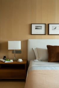 A contemporary bedroom featuring a white upholstered bed with a wooden bedside table, light-colored walls, and framed art on 
