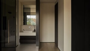 Modern bathroom with a glass countertop and sink, visible through a glass door leading to another room. Light wood flooring a